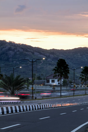 Highway road with motion blurred lights at dusk leading towards mountains and town with a colorful sky providing a scenic travel viewの写真素材