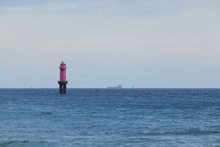 Pink lighthouse standing tall in the ocean under a cloudy sky, guiding ships and ensuring maritime...