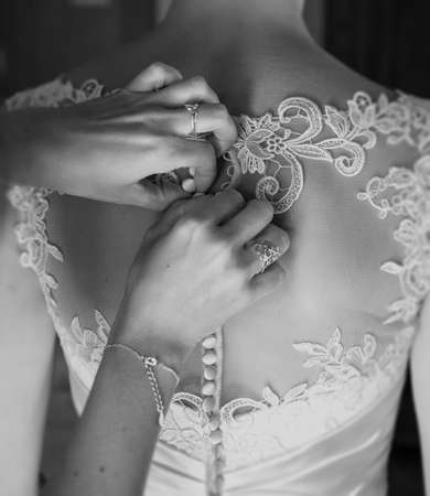 Bridesmaid tying buttons on a Brideの写真素材