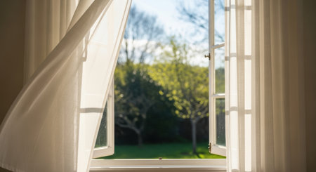 Open window with white curtains and view of the garden in the morningの素材