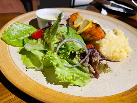 smoked grilled salmon fish served with salad and mash potatoes with lemons on top, served in plate...