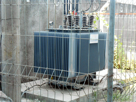 High Voltage Transformer Enclosed Behind Metal Fencing in an Industrial Setting, An image depicting...