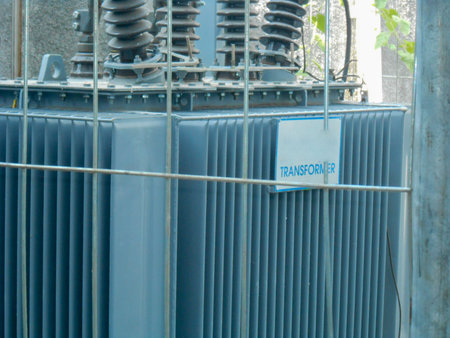 High Voltage Transformer Enclosed Behind Metal Fencing in an Industrial Setting, An image depicting...