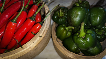 Vibrant red chili peppers and fresh green bell peppers arranged in bamboo bowls creating a colorful...