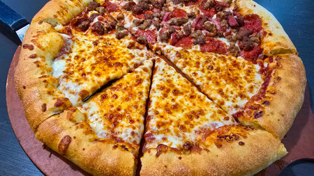 Delicious pizza featuring a combination of cheese and meat lovers toppings, served on a wooden board. The golden cheese stuffed crust and melting cheese emphasize fresh and irresistible flavors, creating a mouthwatering culinary experience.の写真素材