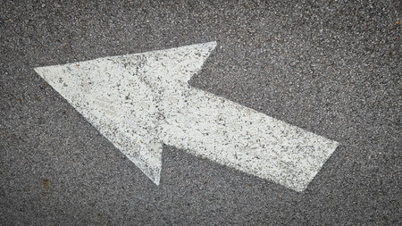 White painted arrow on asphalt road surface, representing direction and navigation in transportation...