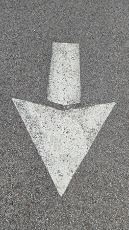 White painted arrow on asphalt road surface, representing direction and navigation in transportation...