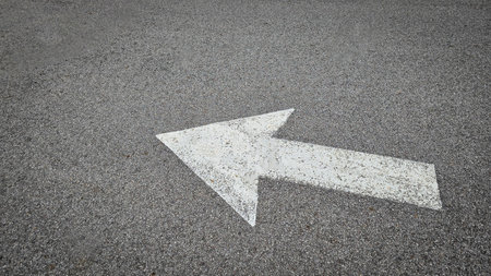 White painted arrow on asphalt road surface, representing direction and navigation in transportation...
