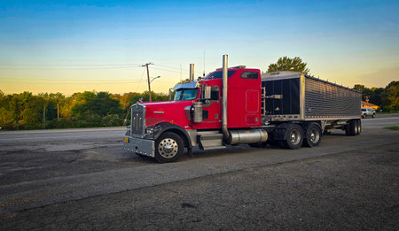 bold red semi truck with a long trailer sits in an open lot during sunset. The powerful rig highlights industrial design, chrome accents, and the rugged appeal of transportation and logistics.の写真素材