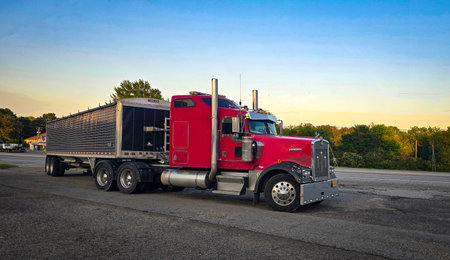 bold red semi truck with a long trailer sits in an open lot during sunset. The powerful rig highlights industrial design, chrome accents, and the rugged appeal of transportation and logistics.の写真素材