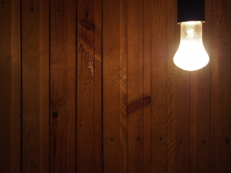 Light bulb hanging from the wall and illuminating the wooden wallの写真素材