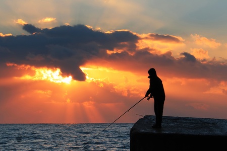 A fisherman on the rock against dawn sky の写真素材