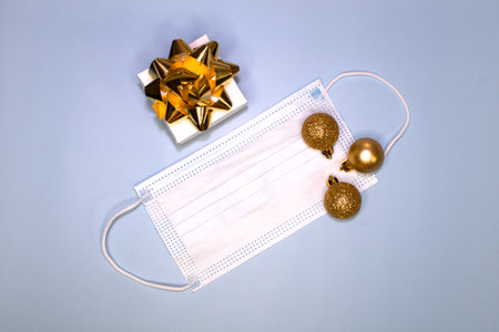 Gift box decorated with a gold bow with balls and a mask on a blue background. Top viewの写真素材
