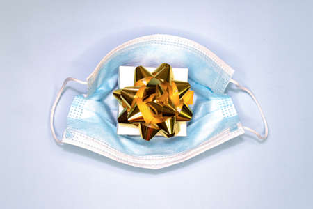 Gift box decorated with a gold bow and a mask on a blue background. Top view