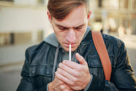 Brutal young man in a black leather jacket lighting a cigaretteの写真素材