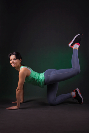 Beautiful sporty woman doing exercise lifting legs on dark background with green backlightの写真素材