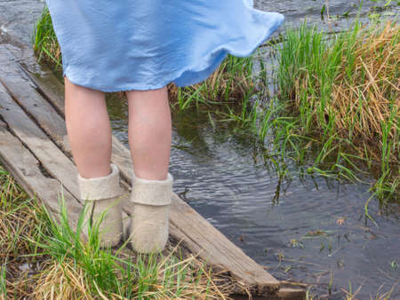 Cold summer. Women's feet in felt boots on the background of green grass and water lakeの写真素材