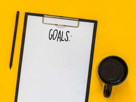 Top view goals list with notebook, cup of coffee on yellow background with blank space for text....