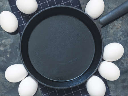 Black cast-iron frying pan on black cloth, white chicken eggs. Black background with blank space for text. Top view. Copy space.の写真素材