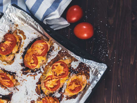 Chicken fillet baked with tomatoes and cheese on a baking sheet with foil. Delicious healthy food. Lifestyle. Flat lay. Top view. Wooden backgroundの写真素材