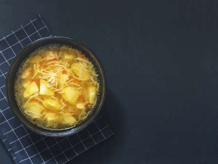 Chicken soup with potatoes, noodles, onions, carrots on black background. Top viewの写真素材
