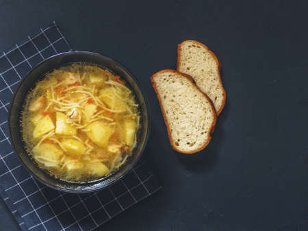Chicken soup with potatoes, noodles, onions, carrots and two pieces of bread on a black background. Top viewの写真素材