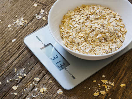 Grits in a white bowl on the kitchen scales on wooden background. Product weighing