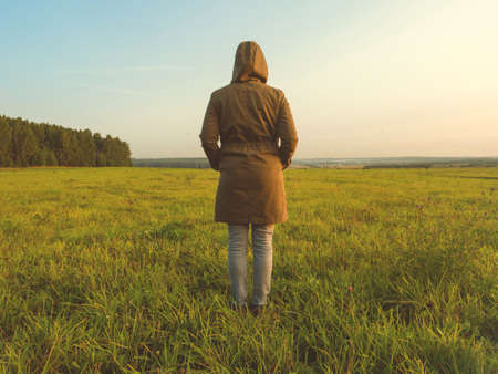 Girl in a windbreaker stands back in the field in autumnの写真素材