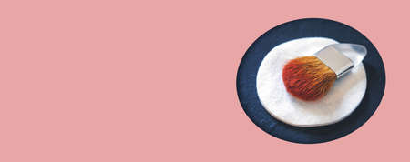 The makeup brush and round white cotton pad on a black background in a hole in pink paper. Makeup...