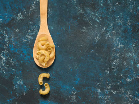 Dry pasta in wooden spoon on blue grunge background. Top view. Copy spaceの写真素材