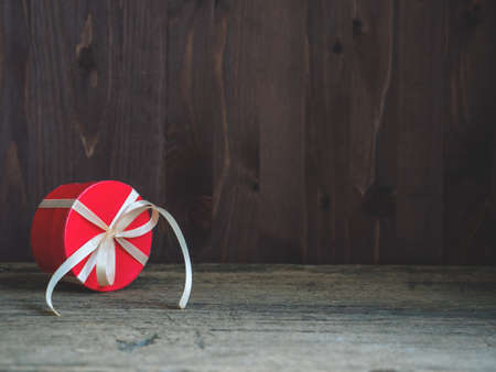 Round red gift box wrapped with festive ribbon on wooden background. Copy spaceの写真素材