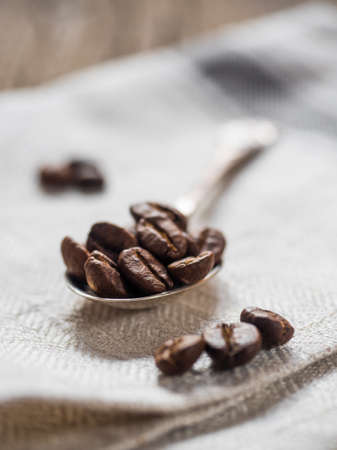 Coffee beans in a silver spoon on a gray canvas closeupの写真素材