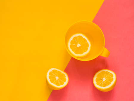 Creative fresh layout. Water with lemon in a yellow mug on a yellow and pink geometric background.の写真素材