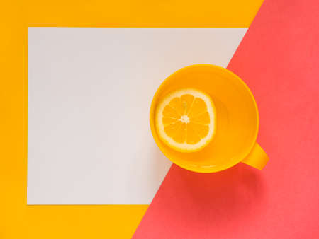 Creative fresh layout. Water with lemon in a yellow mug on a yellow and pink geometric background.の写真素材