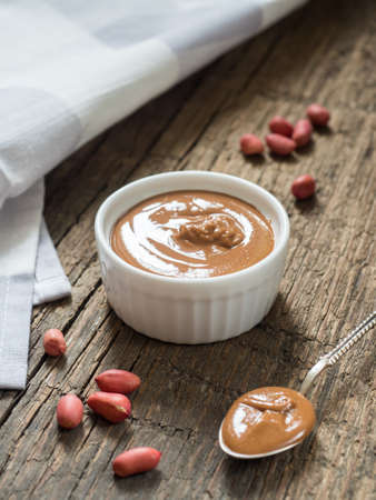 Peanut butter in a white bowl on a wooden table. Natural healthy nutrition and organic food
