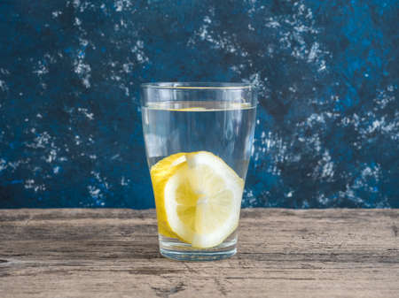 Fresh clean water in a glass with slices of lemon. Lemonade on wooden table and blue background.