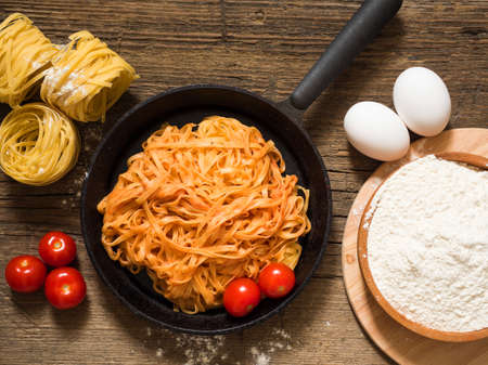 Appetizing traditional classic Italian pasta with tomato sauce and basil in a black frying pan on a wooden table. Flat layの写真素材
