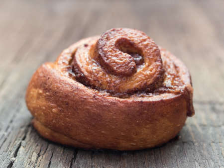 Confectionery baking. Sweet fresh soft roll bun with cinnamon on wooden background. Cinnabon closeup
