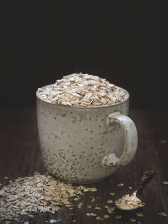 Healthy food concept. Dry oat flakes spilled from a gray ceramic cup onto a wooden table. Closeup
