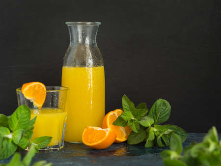 Healthy fruit drink. Natural fresh squeezed orange or tangerine juice in a glass bottle with water drops and fresh green mint on a dark background.の写真素材