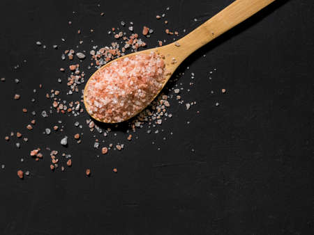 Healthy spices concept. Large dark pink himalayan salt in a wooden spoon and spilled on a black...