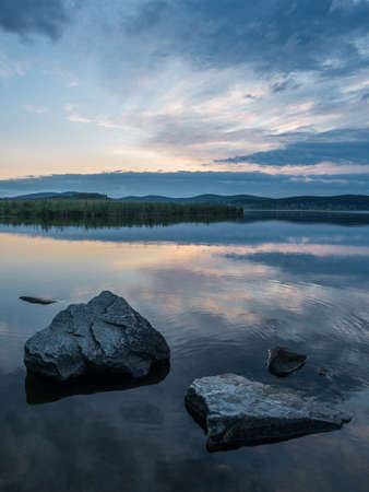 Calm, serenity, meditation concept. Sunset on the lake, stones in the water in the foreground, quiet water, cloudless sky.の写真素材