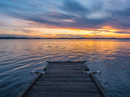 Sunset on the lake, wooden bridge in the foreground, cloudless sky.の写真素材