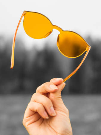 Colorized lifestyle concept. Orange sunglasses in a female hand on a gray backgroundの写真素材