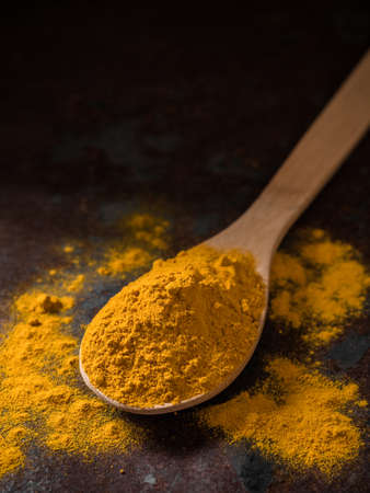 Turmeric powder. Traditional indian golden healthy spice in wooden spoon on dark background
