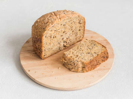 Half a loaf of homemade whole grain bread with various seeds and two slices on a white background....