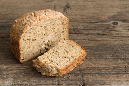 Half a loaf of homemade whole grain bread with various seeds and two slices on a wooden background....