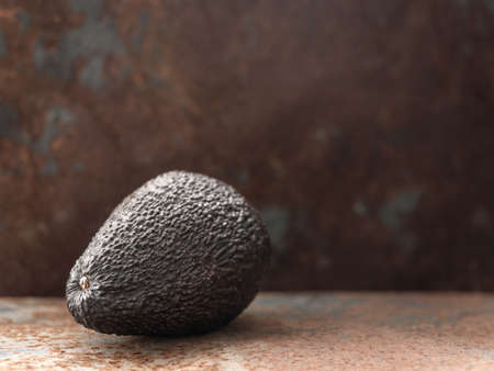 Whole ripe brown hass avocado fruit on dark table. Healthy fats. Side view, copy space.の写真素材