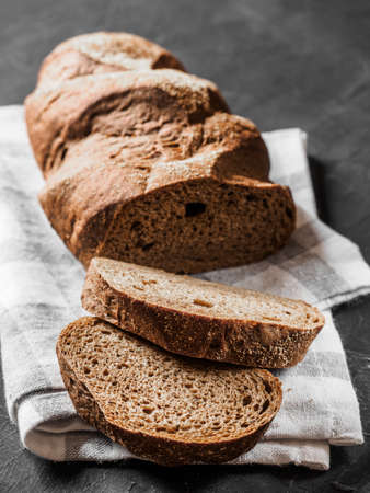 Loaf dark buckwheat bread on white textile napkin black table background. Fresh delicious homemade...