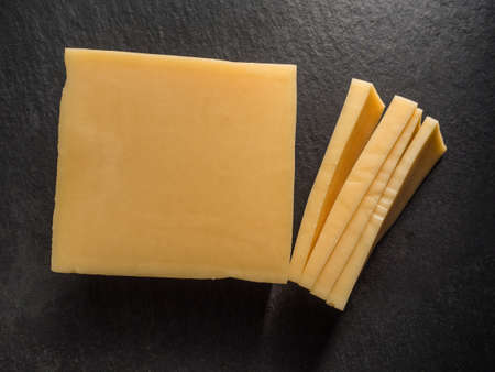 Rectangular sliced parmesan cheese on a black slate cutting board. Close-up